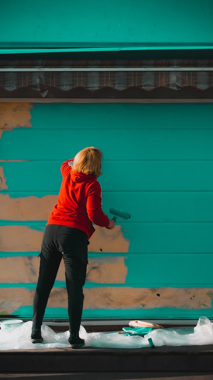 Person in red sweater painting a large wall with a roller brush, showcasing DIY home improvement.
